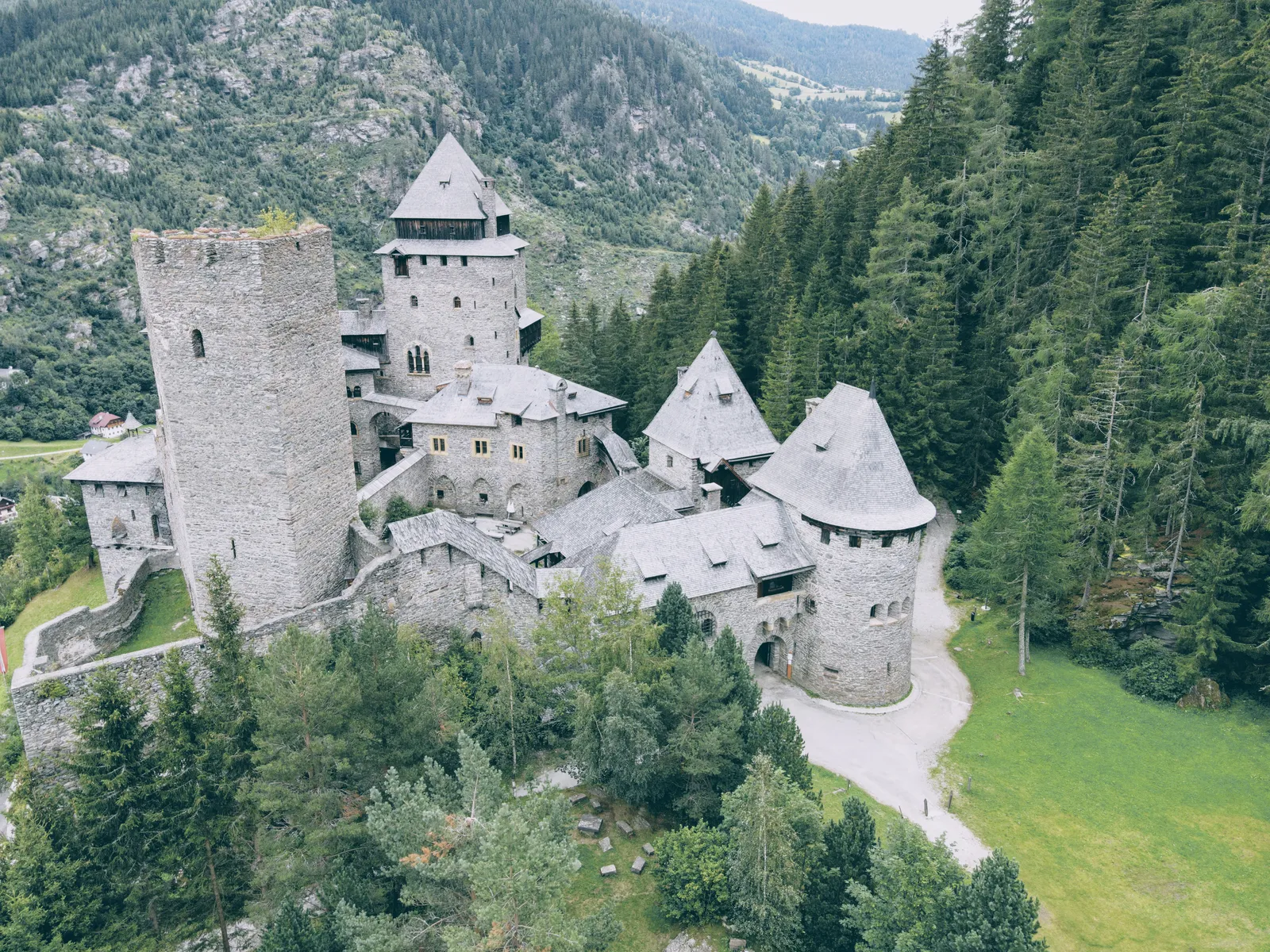 Aerial view of a medieval castle surrounded by forest and mountains