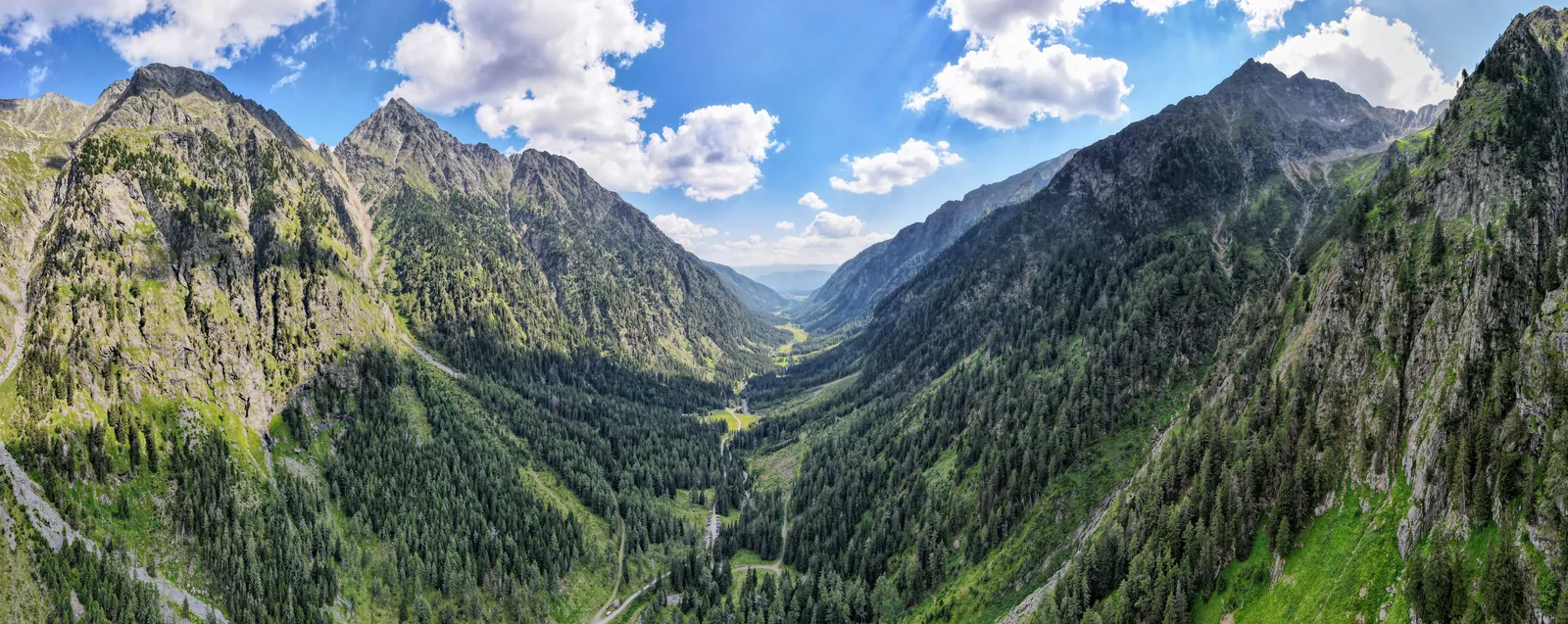 Wide alpine valley panorama with steep mountains and forested slopes