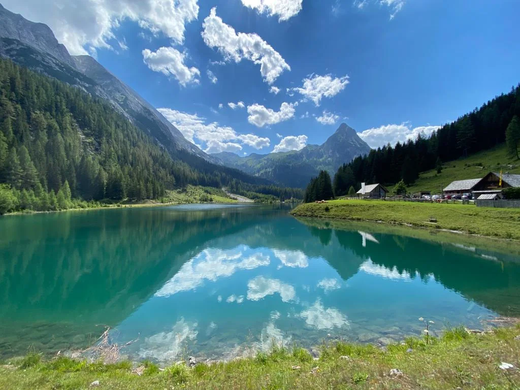 Turquoise mountain lake with forested slopes and cloud reflections near Zederhaus