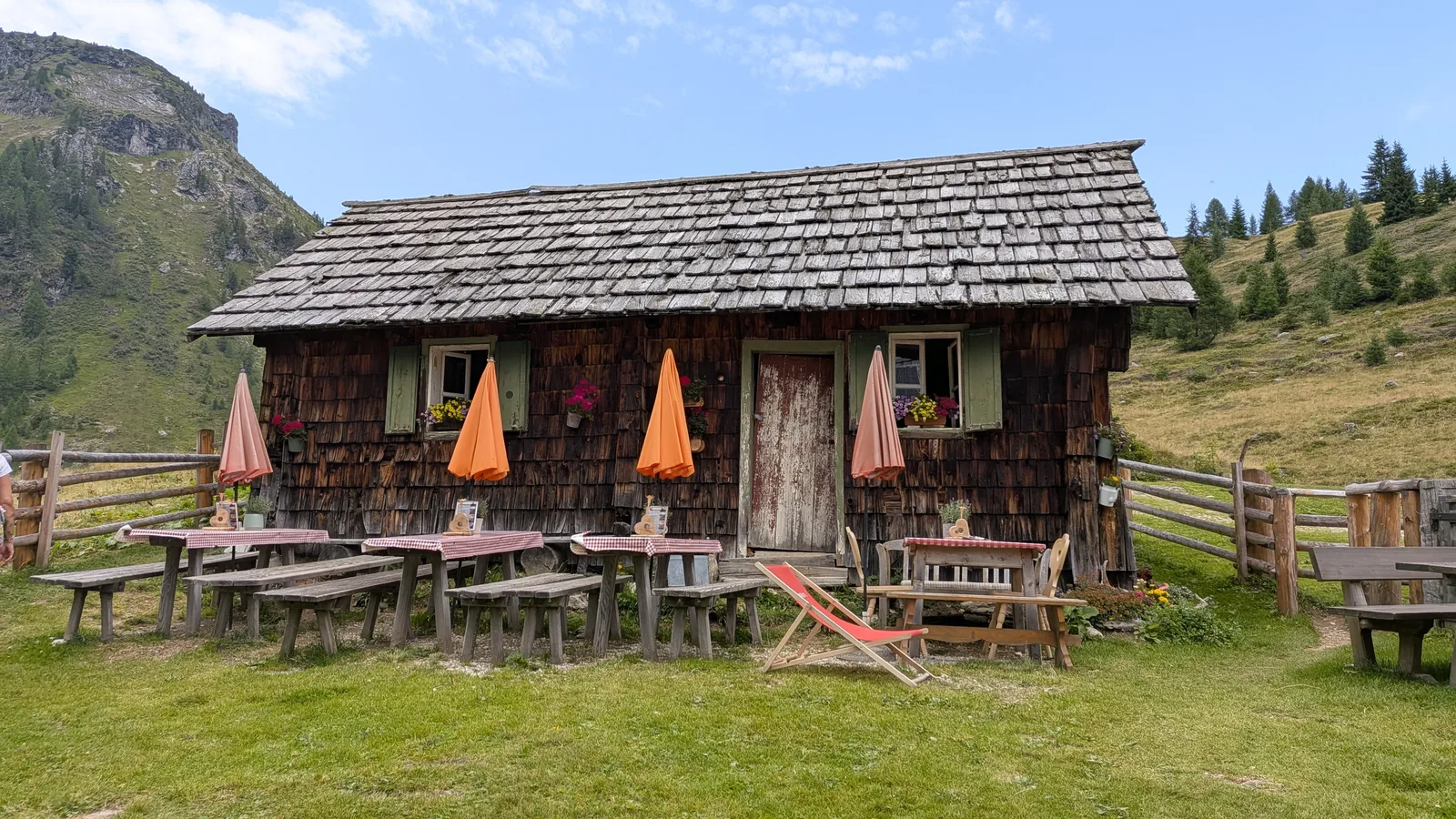 Tonimörtlhütte wooden mountain hut with outdoor tables and alpine slopes in summer.