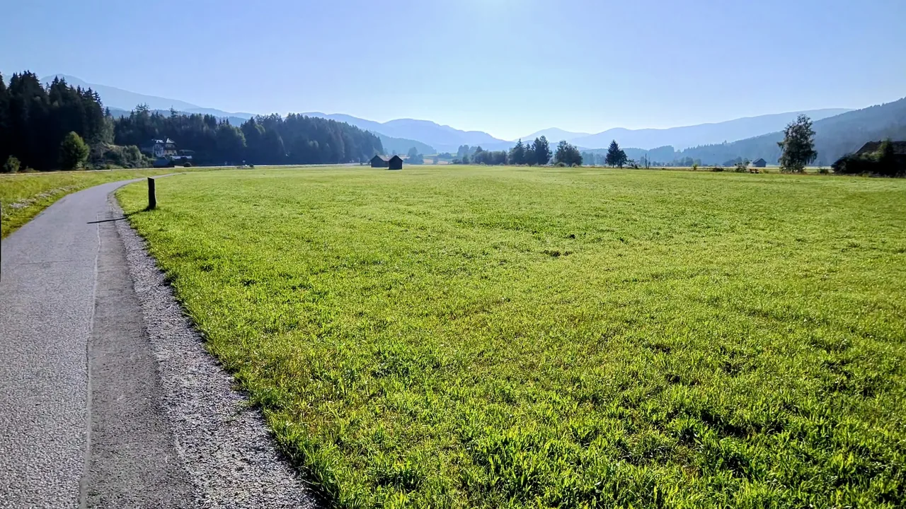Sunny valley road through green meadows near Mariapfarr with mountains in the distance.